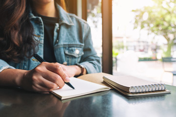Closeup image of a woman writing on a blank notebook on wooden table