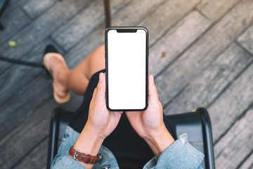 Top view mockup image of a woman holding a black mobile phone with blank white desktop screen - obrazy, fototapety, plakaty