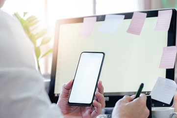 Closeup man using smartphone with blank screen while sitting at office desk, blank screen for text or graphic design.