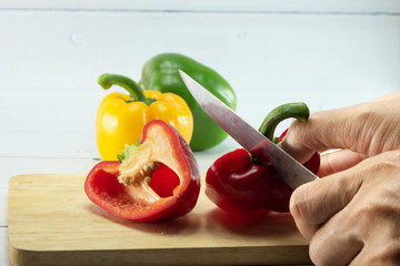 Closeup of woman's hand slicing Red, Yellow, Green, bell pepper or sweet pepper or capsicum on chopping wood on white background with selective focus,raw food ingredient concept.
