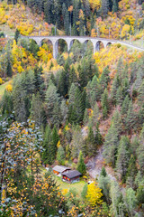 Chalets deep in the colorful forest in autumn season in the mountain with the Albula railay bridge...