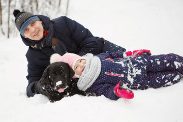 Fototapeta na wymiar Man and girl fun with his black labrador retriever in winter forest.