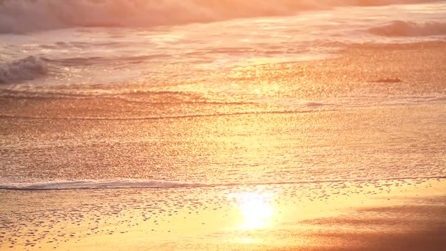 Slow-motion pan up of beach and waves at sunset in California