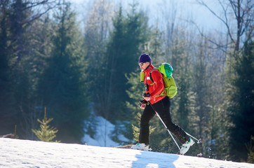 Strong sportive male skier tourist with backpack in sunglasses walking on skis uphill in snow on...