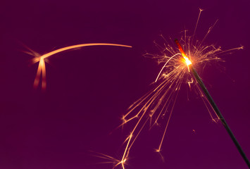 Burning christmas sparkler on purple background  close up