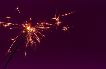 Burning christmas sparkler on purple background with copy space