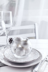 Place table setting on white table with Christmas decor elements. Silver color