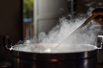 Cooking person in the restaurant is cooking while using the dipper in a large pot. And the water is boiling.