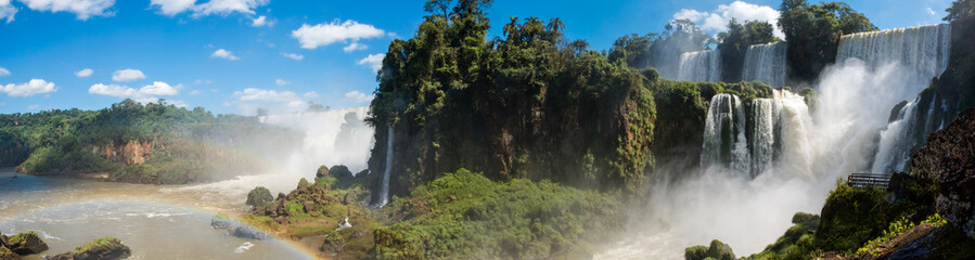 A panoramic of the famous Iguazu Falls with many waterfalls gushing water on the a sunny day. 