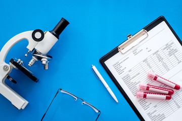 Blood test results near microscope on blue background top view