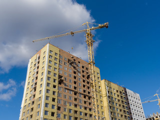 Fototapeta premium A tower crane is building a high-rise apartment building of brick. The walls are insulated. The theme of an emerging housing market under construction