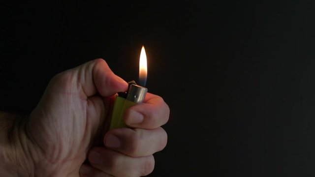 Close view of hand holding a lighter and lighting it with a black background. Close up of lighter.