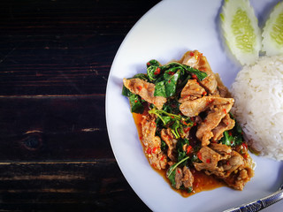 Stir fried beef basil with steamed rice With cucumber as a side dish Put on a white plate Basic Thai food. Ingredients are garlic, fresh chilies, basil leaves and meat.