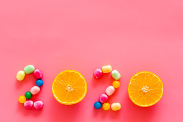 Sweet New Year design. 2020 laid out with candy and oranges on pink background top view copy space