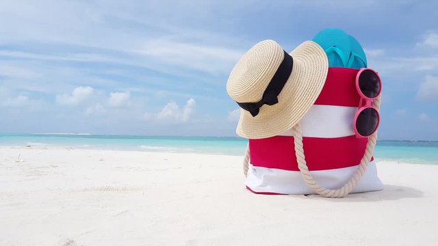 Abstract concept, beach bag with straw hat and pink sunglasses on tropical beach in Hawaii, with white sand, with waves gently breaking over the shore