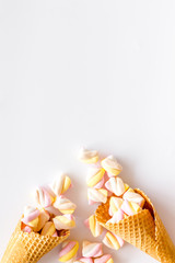 Sweet desserts. Marshmallows in ice cream waffle cone on white background top view copy space