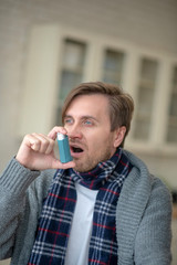 Blue-eyed young man having asthma using inhalator