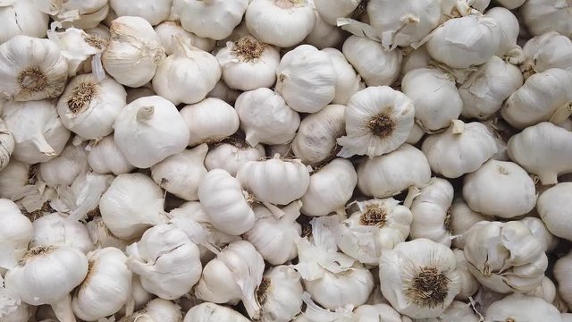 Slow motion zoom in over a pile of white garlic bulbs, allium, sativum, on display on a market stall