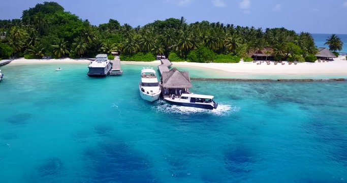 Large white motor boats docked on a tropical island with clear bright teal water and lush forest in the background in the Maldives