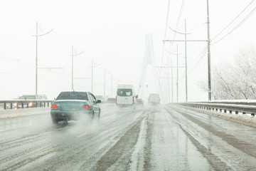 Cars drive along road with slush, snowstorm. City traffic in snow blizzard.