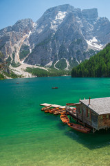 Naklejka premium view of wooden house on water with pier and boats lake in dolomites mountains