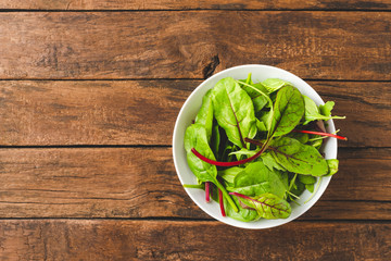Overhead shot of fresh green salad with spinach, arugula and beetroot leaves in bowl on old wooden background with copyspace