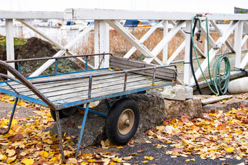 Old wheelbarrow with rubber wheels and autumn leaves. Wooden white fence.