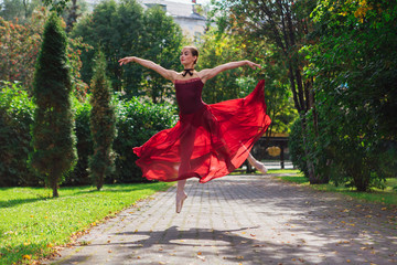 Woman ballerina in red ballet dress dancing in pointe shoes in autumn park.