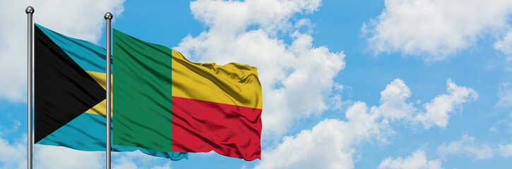 Bahamas and Benin flag waving in the wind against white cloudy blue sky together. Diplomacy...