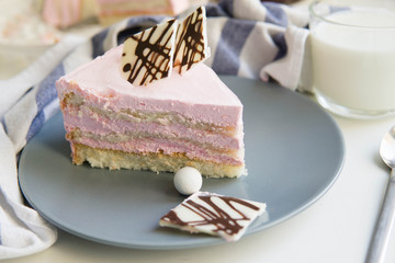 A piece of cake with pink strawberry cream and biscuit and chocolate on it with a cup of milk)