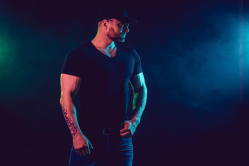 Naklejka premium Young strong man bodybuilder in cap on wall background. Dark dramatic colors. Smoke on background.