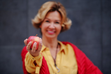 Beautiful healthy blonde fashionable senior woman holding apple. Selective focus on hand.