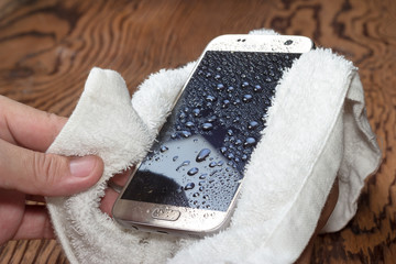 Hands holding White cloth with wet smartphone drops on wooden floor