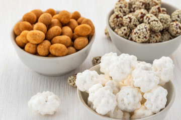 Peanuts in sugar, peanuts sprinkled with sesame seeds and peeled peanuts lies in three white bowls on a white wooden background, side view from above
