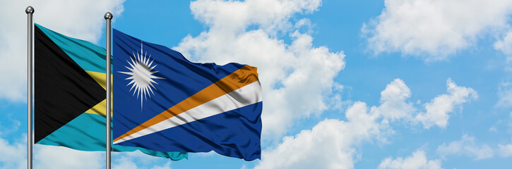 Bahamas and Marshall Islands flag waving in the wind against white cloudy blue sky together. Diplomacy concept, international relations.