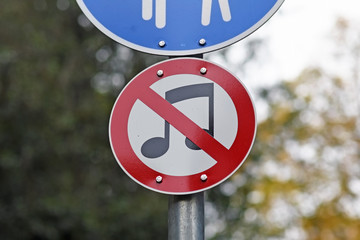 Unusual round street sign with music notes crossed out in red forbidding playing or listening to...