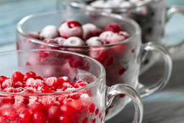 Ripe frozen sweet cherries, red currant and black currant with hoarfrost in the transparent glass cups on blue wooden background. Natural organic healthy food. Closeup, selective focus