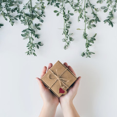 Woman packing gift in a box of kraft paper on white wood table. Green leaves, branches. concept....