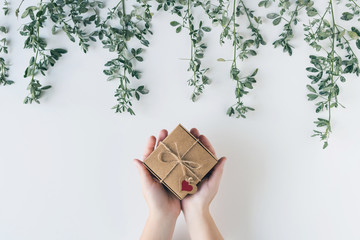 Woman packing gift in a box of kraft paper on white wood table. Green leaves, branches. concept....