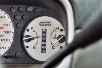 Car dashboard with text Unleaded fuel only. Fuel level and temperature gauges close-up