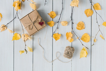 Woman packing gift in a box of kraft paper on white retro wood boards. leaves, birch branches. Thanksgiving. Autumn, fall concept. Flat lay, top view.