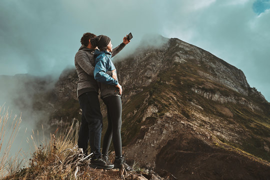 a young, happy couple hugges on a cliff and takes a selfi photo