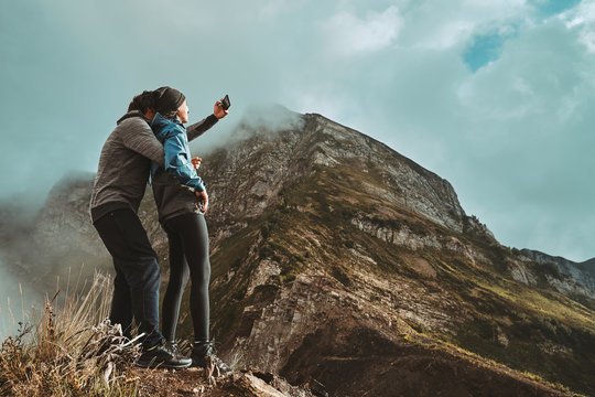a young, happy couple hugges on a cliff and takes a selfi photo