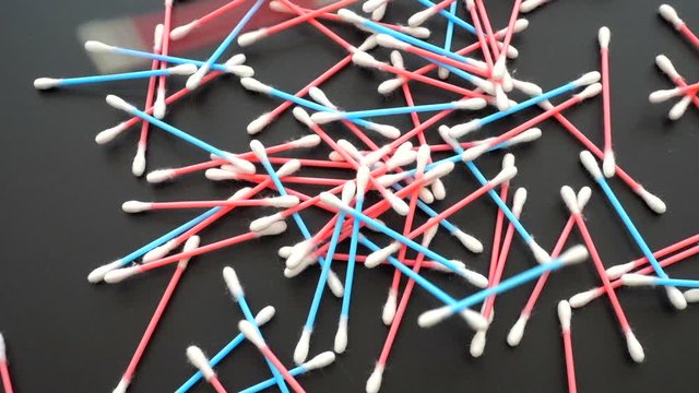 Close POV shot of pink and blue cotton swabs / buds falling onto a table.