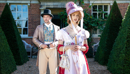 Handsome man and beautiful woman dressed in vintage clothing, standing in front of stately home