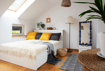 Cozy bedroom in bright apartment with double bed and modern design in scandinavian style. White and grey decor and yellow pillows on a bed in the attic.