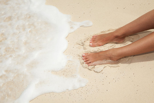 Summer beach concept. Care for beautiful woman skin and nails. Woman legs, spa therapy. Closeup photo of sandy female feet with white french pedicure on the beach background.
