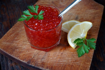 Delicious red caviar in a glass served with parseley and lemon on wooden desk.
