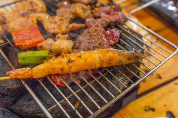 Shrimp and assortment of meat grilling on flaming charcoal stove