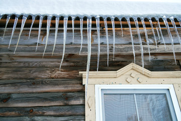 Large dangerous icicles hanging on the roof of a wooden country house in winter or spring in Russia.